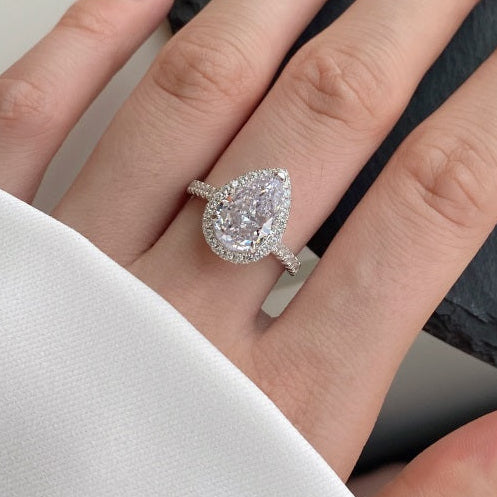 Pear-shaped diamond ring on a hand against a neutral background