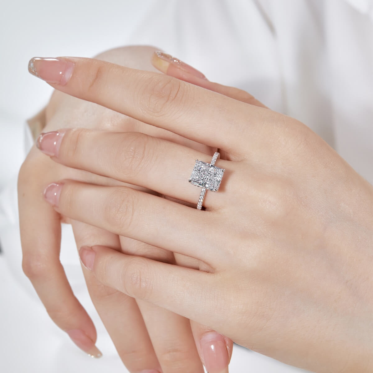 A silver ring with a large rectangular cubic zirconia stone surrounded by a smaller halo of stones, worn on a hand.