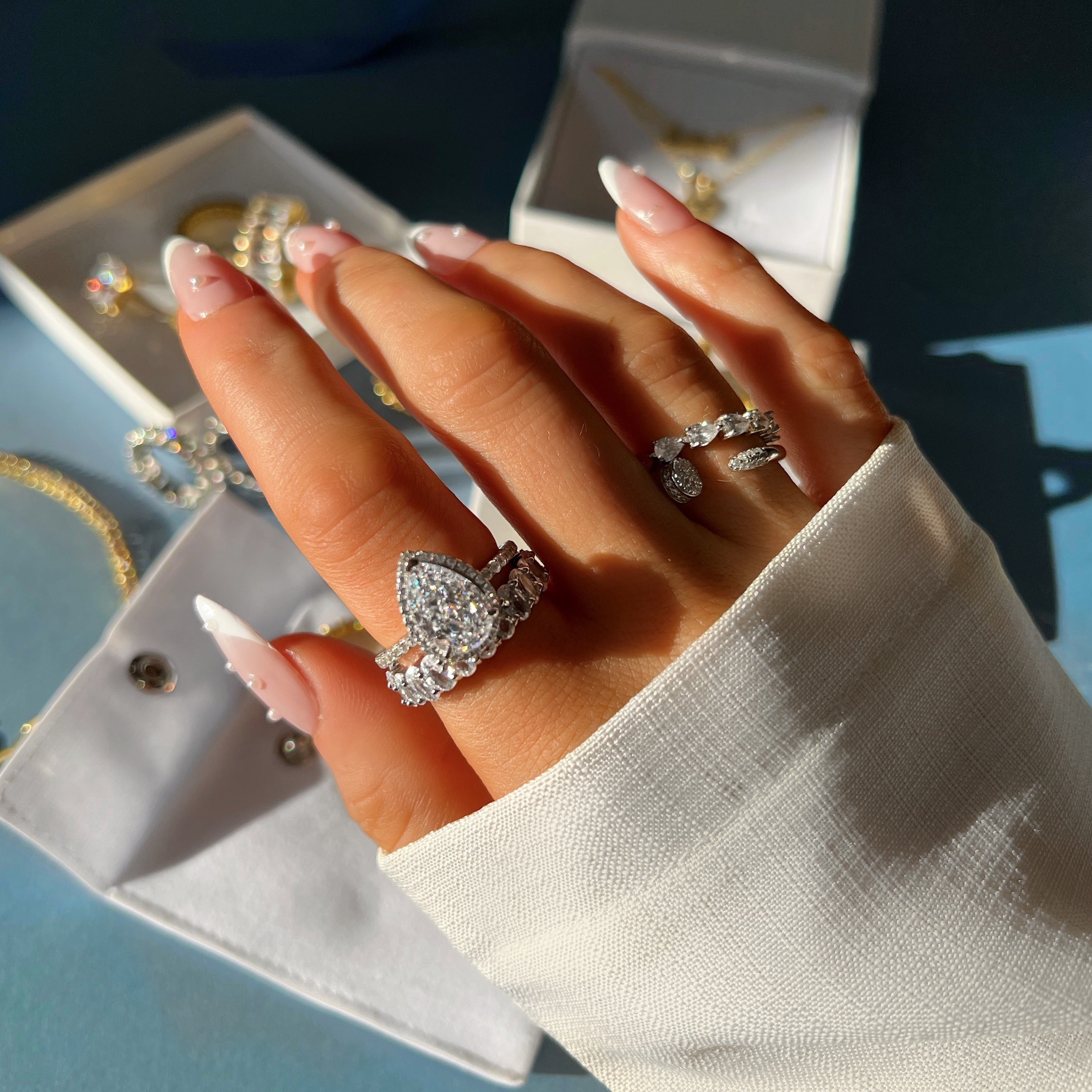 A close-up of a pear-shaped diamond engagement ring with a sparkling halo, set in a silver band. With other stacking rings on a hand