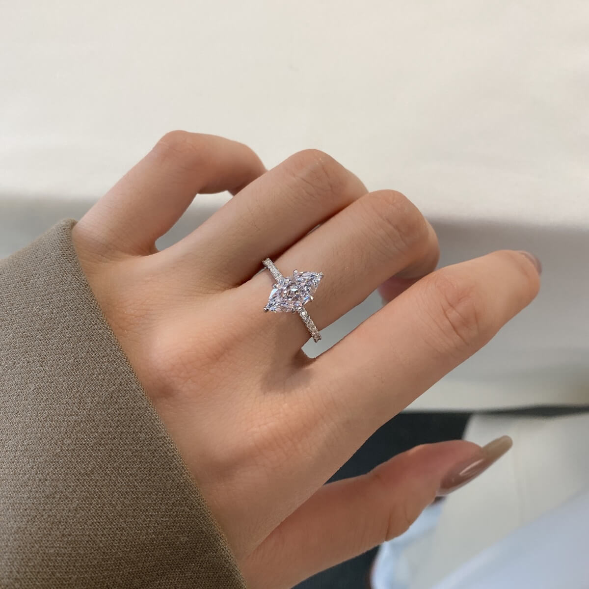 A marquise-shaped Cubic Zirconium ring with smaller stones set in a semi-full pavé band, with a champagne gold finish on a hand.